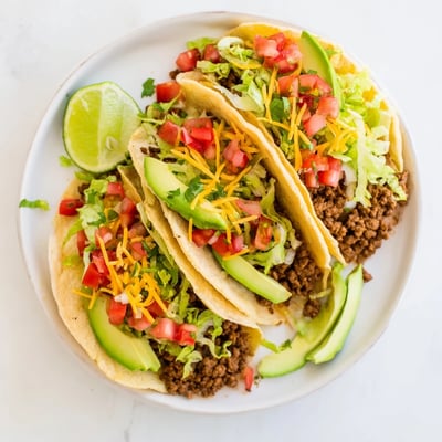 Juicy seasoned ground beef tacos garnished with vibrant pico de gallo avocado slices and crisp shredded lettuce