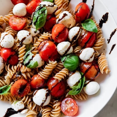 Colorful Caprese Pasta Salad featuring fresh basil leaves, juicy tomatoes, and tender penne pasta